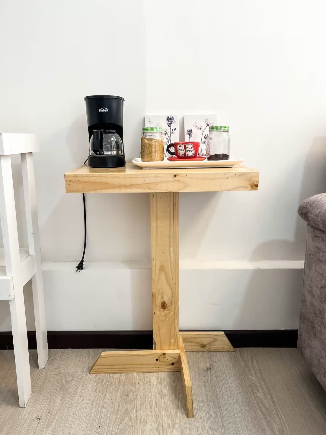 Rincón de Café: Una mesa de madera clara con una cafetera negra y frascos decorativos. Hay tazas rojas y tarros de cristal, creando un espacio ideal para disfrutar de un café.